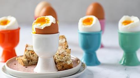 Dipping eggs in colourful egg cups with toast